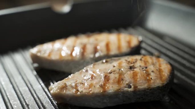 新鲜的三文鱼排在油锅中油炸。在黑色背景上