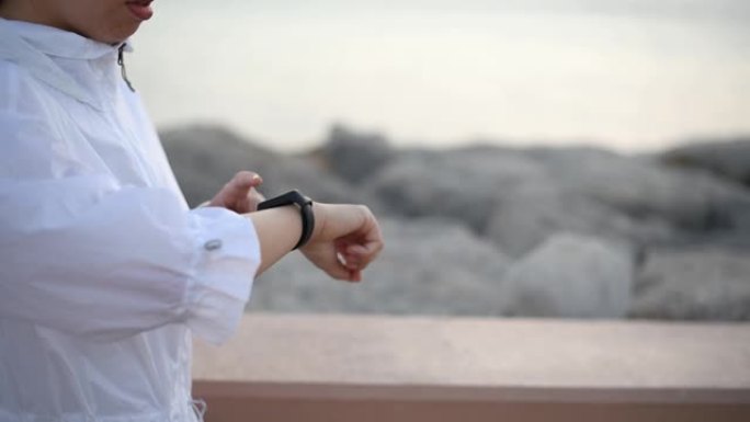 女人在日落时使用智能手表健身跟踪器和计步器在海边跟踪户外锻炼
