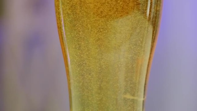 淡淡的啤酒放在蓝色模糊背景上的玻璃杯中。在一杯啤酒中沸腾气泡。精酿啤酒概念。慢动作。特写