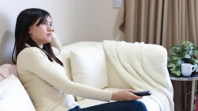 年轻的亚洲女球迷坐在沙发上看电视上的体育比赛，在家欢呼
