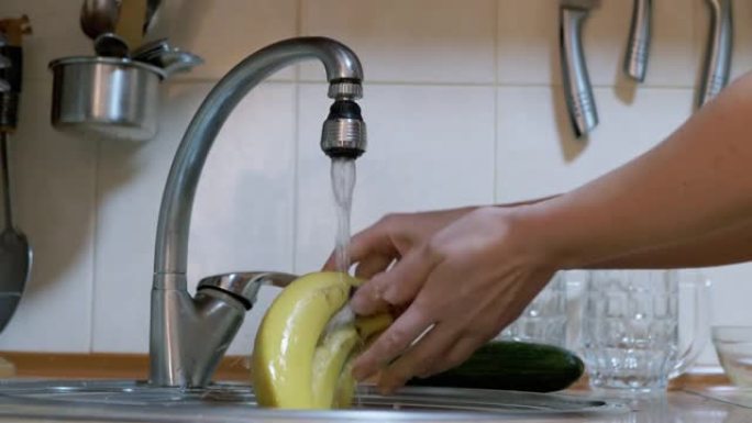 女人打开水龙头，在水槽里洗黄瓜，香蕉，苹果，关掉水