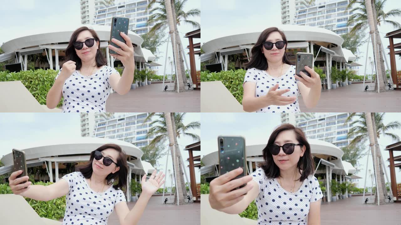 快乐的亚洲女人在游泳池边放松，在酒店度假期间用智能手机自拍照片，生活方式概念。