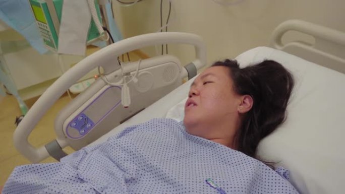 年轻的亚洲华裔女士在医院病床上收缩疼痛等待分娩