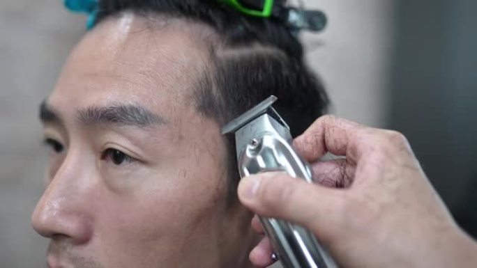 特写，亚洲中国男性理发师在沙龙里用理发推子刮男人的头发。理发店。