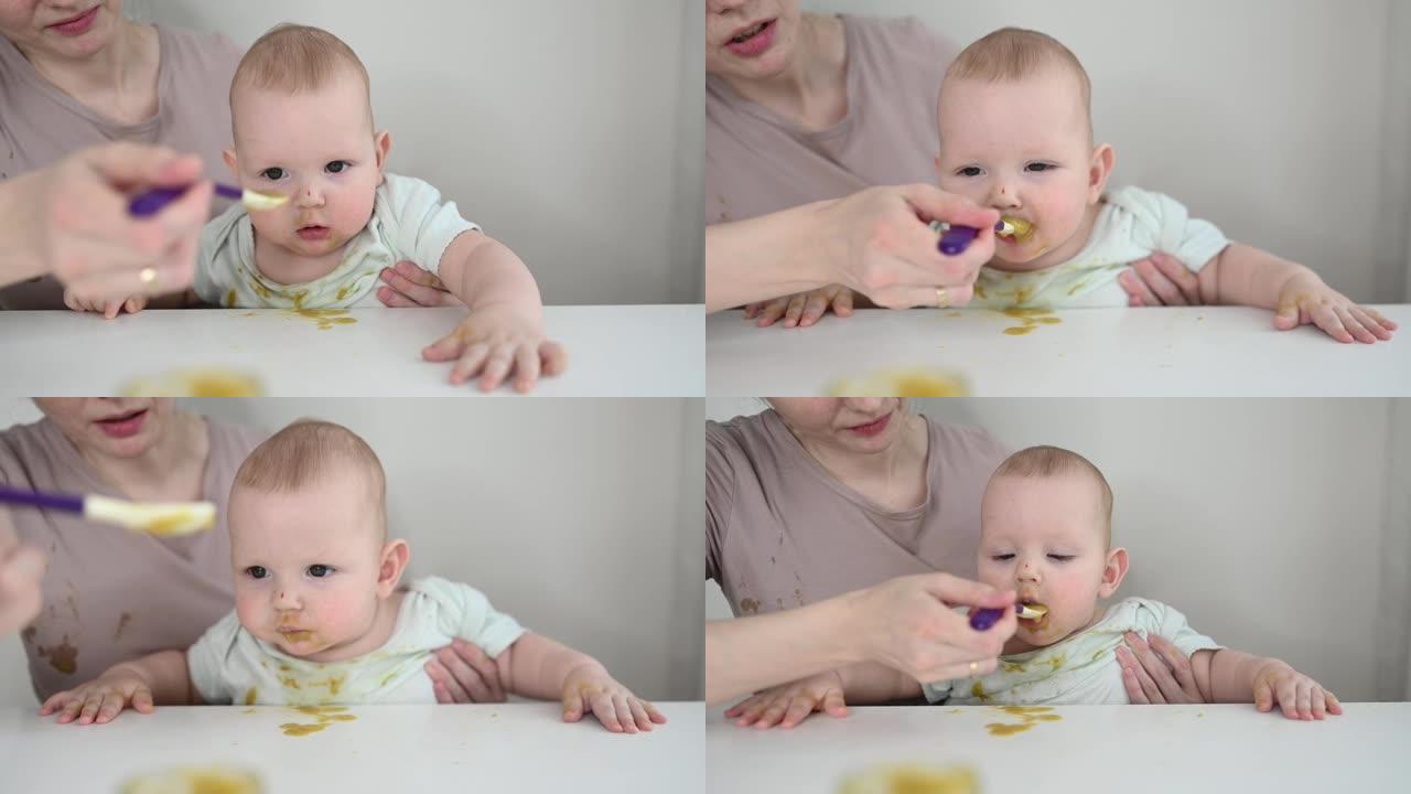 刚出生的有趣的小男孩正在学习用勺子从玻璃罐里吃蔬菜或水果泥。年轻的母亲帮儿子吃第一顿饭。