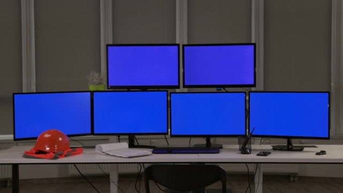 工程师工作场所。六个电脑屏幕。在桌面橙色头盔和背心上。