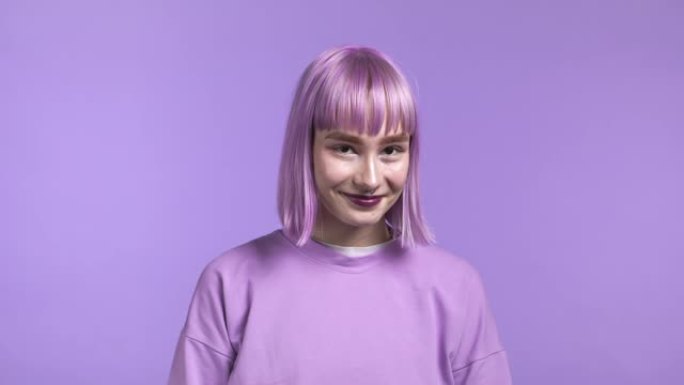 紫色工作室背景上染紫罗兰色头发的时髦女人肖像。积极的年轻派对女孩看着镜头。令人惊叹的化妆和迷人的微笑