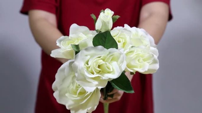 闭合女性双手，手持五颜六色的玫瑰花束。女人手触摸玫瑰花蕾叶，白色针织毛衣背景。