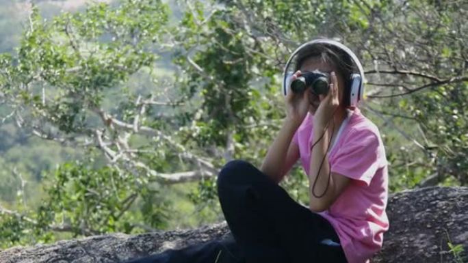 亚洲女孩坐在山顶上使用双筒望远镜，生活方式的概念。