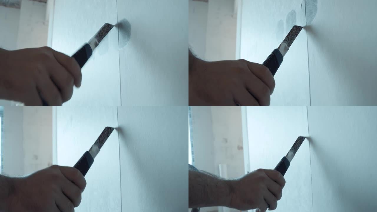 男性手持金属刀切割玻璃纤维粘在墙上的接缝。壁纸裁剪，表面调平