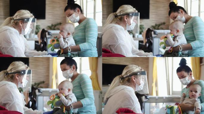 穿着防护服和遮阳板的儿科医生正在和婴儿玩耍。女医生上门探望母婴