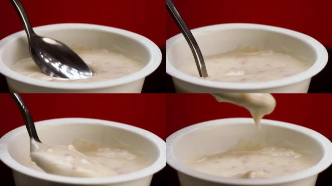 用勺子从塑料罐里吃谷类酸奶。库存镜头。在红色背景上隔离的希腊酸奶的特写镜头，健康的早餐或小吃
