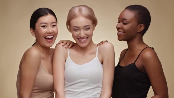 国际友谊。快乐的亚洲、高加索和非裔美国女士一起笑，米色工作室背景