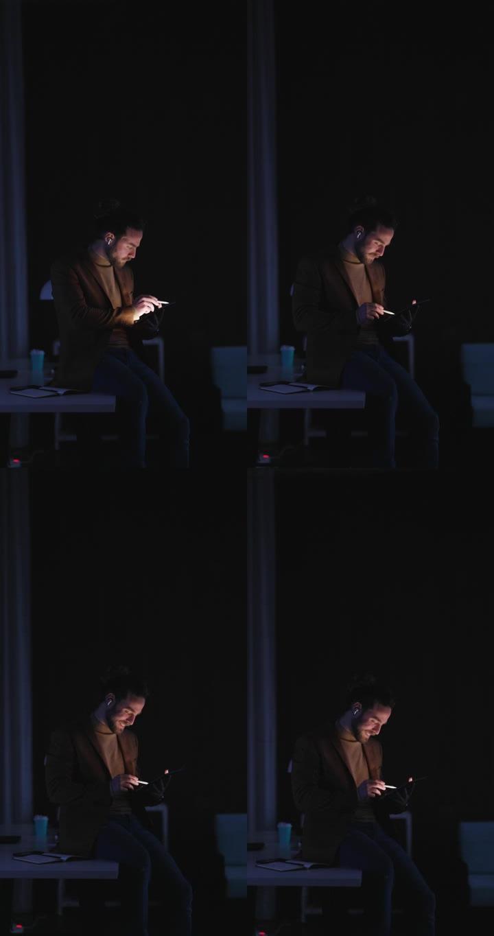 在工作的深夜里，英俊的商人坐在办公室的桌子上，使用数字平板电脑