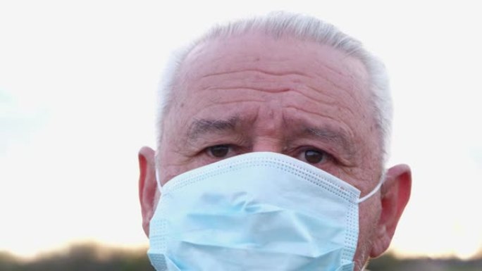 一个戴着医用口罩的老人看着相机。