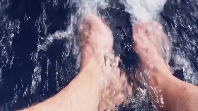 在阳光明媚的日子里，赤脚从船上放下，成年男子的脚，蓝色的水，飞溅和气泡，以极快的速度运动