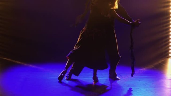 一对舞厅舞者表演的古典华尔兹舞蹈的元素。搭档华尔兹牵手。在黑暗的工作室里拍摄，背景是蓝色的灯光。特写