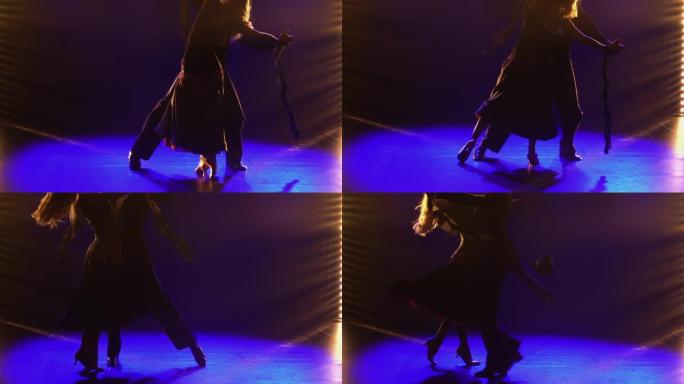 一对舞厅舞者表演的古典华尔兹舞蹈的元素。搭档华尔兹牵手。在黑暗的工作室里拍摄，背景是蓝色的灯光。特写