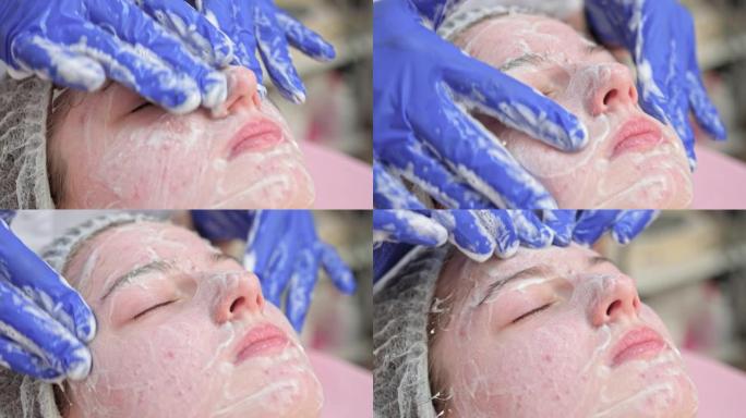 美容师医生正在美容诊所将面部清洁泡沫应用于女性面部按摩皮肤。美容师在美容院制作护肤程序，年轻女子肖像