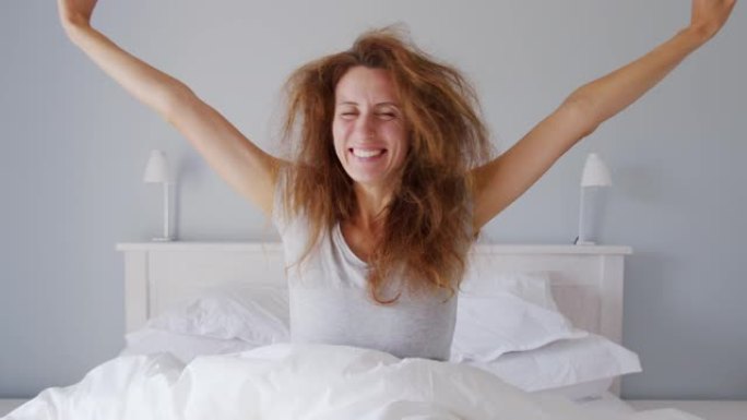美丽的女人早上醒来感到精神焕发和快乐。充足的睡眠有助于保持你的健康。清洁卧室没有细菌和疾病。