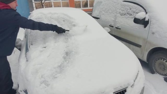 男人用雪刷擦车。冬天暴风雪过后，人们在汽车上刷新鲜的雪。冬季寒冷天气车主的困难