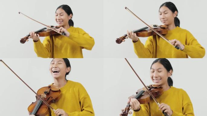 笑着的亚洲女学生穿着黄色毛衣学习拉小提琴与灰色背景，生活理念。