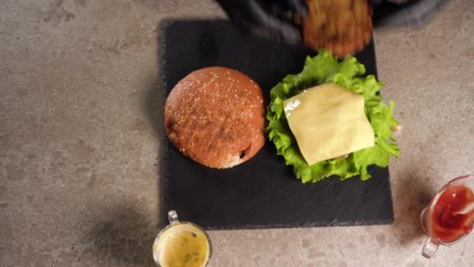 厨师准备三明治。厨师的手准备一个美味的双汉堡的特写镜头，将牛肉饼放在切达干酪上。平躺。