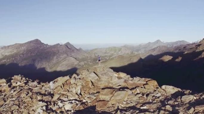 年轻人徒步登山的圆形鸟瞰图日出时在山顶上看全景。站在岩石最高峰山顶上的男人的自由感。蓝色t恤，靴子，