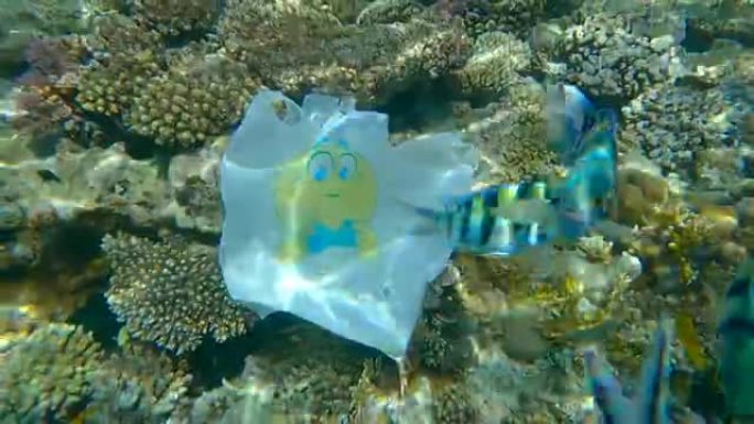 黄色笑脸的塑料购物袋在美丽的珊瑚礁附近漂流，周围有热带鱼。塑料垃圾环境污染问题。(4K-60fps)