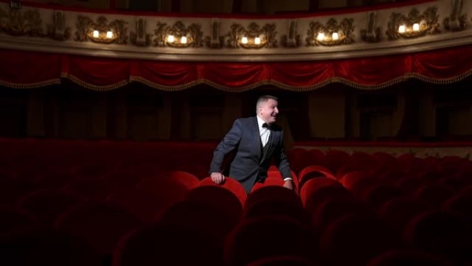 男人独自站在经典剧院的维莱维特椅子上。穿着经典西装的男性邀请公众进来。演出前的时间。
