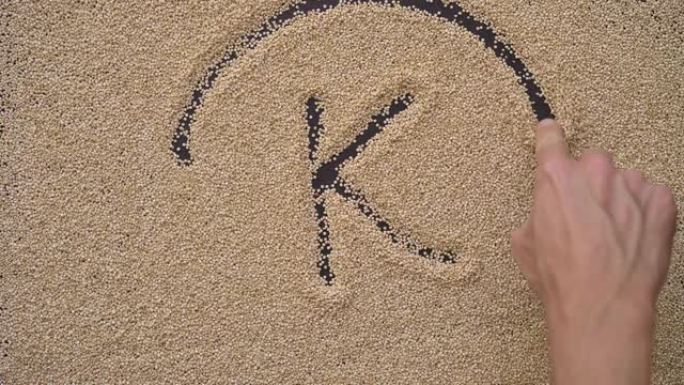 一个人用藜麦种子在黑色背景上写文字。他将文字K写成钾微量元素的符号