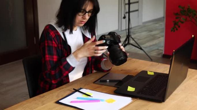 摄影师女性在创意办公室里工作，拿着相机，在桌子上润饰照片