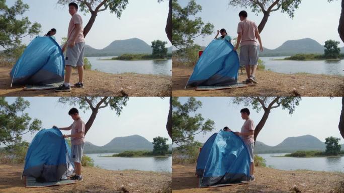 亚洲儿童试图在户外湖泊附近的地面上搭蓝色帐篷，生活方式概念。