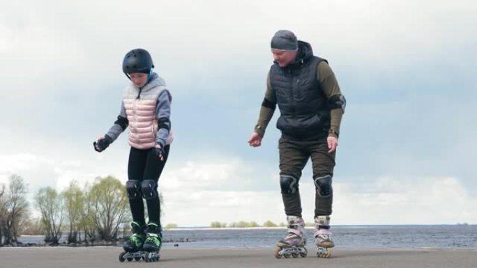 户外轮滑。在户外溜旱冰。十几岁的女孩在父亲的帮助下学习轮滑。周末，爸爸在海滩旁的一条小路上教女儿在户