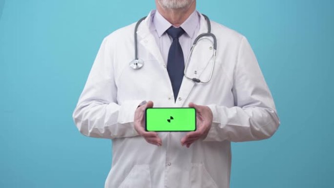 穿着医疗礼服的男士医生会显示带有应用程序的手机屏幕，特写镜头。听诊器制服的医生用手拿着电话，绿屏
