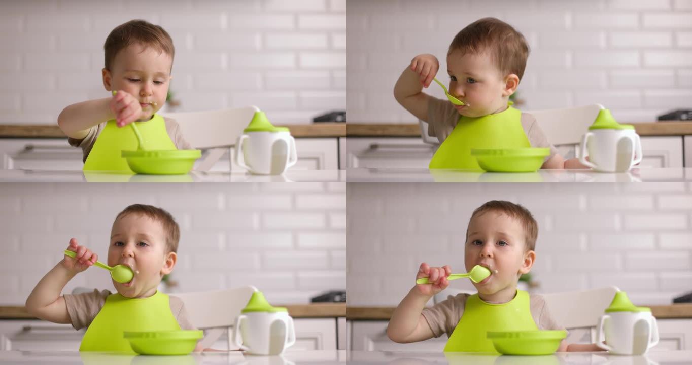可爱的小男孩坐在桌子旁，用勺子吃燕麦片。宝宝在家心甘情愿地吃东西。概念快乐童年