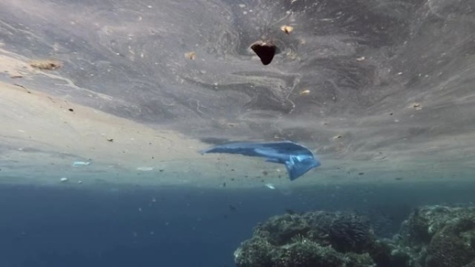 从船上扔出的塑料和其他家庭杂物沿着接近珊瑚礁的水面缓慢漂移。海洋的大规模斑块污染。慢动作，水下拍摄