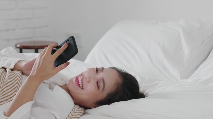 美女躺在床上看手机微笑青年网络生活方式