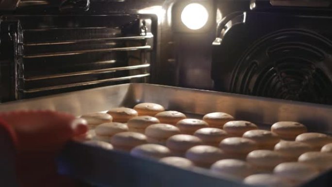 面包师打开烤箱门，取出煮熟的马卡龙。面包师在热食上使用硅胶手套