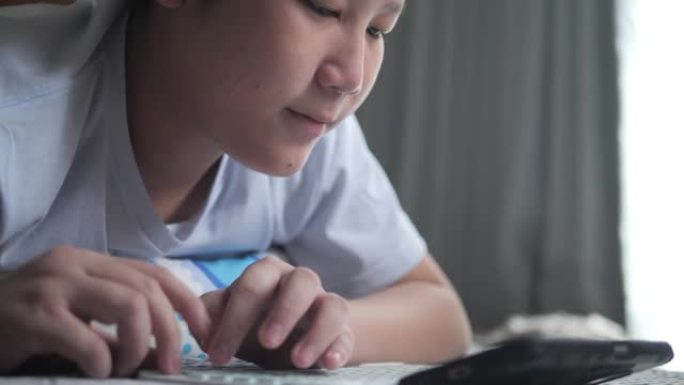 亚洲男孩躺在地板上，在家通过智能手机和无线键盘玩网络游戏，生活方式概念。