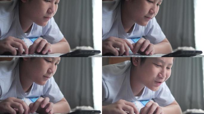 亚洲男孩躺在地板上，在家通过智能手机和无线键盘玩网络游戏，生活方式概念。