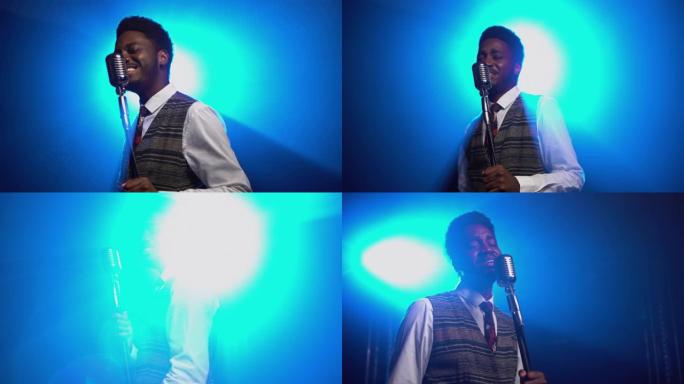 穿着时髦西装的非裔美国人在复古麦克风上唱歌。爵士乐歌手在明亮的蓝色灯光的黑暗工作室中表演。非洲民族音