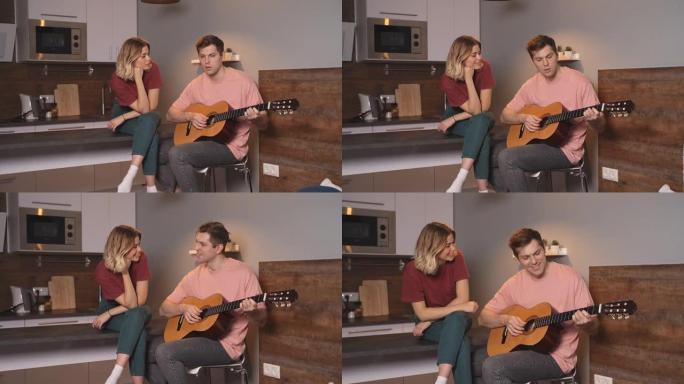 年轻人弹吉他，给坐在家里厨房的女朋友唱一首歌。冠状病毒大流行导致的在家自我隔离的概念