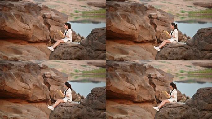 年轻的亚洲女性旅行者坐在泰国大峡谷岩石悬崖上看着纸质地图