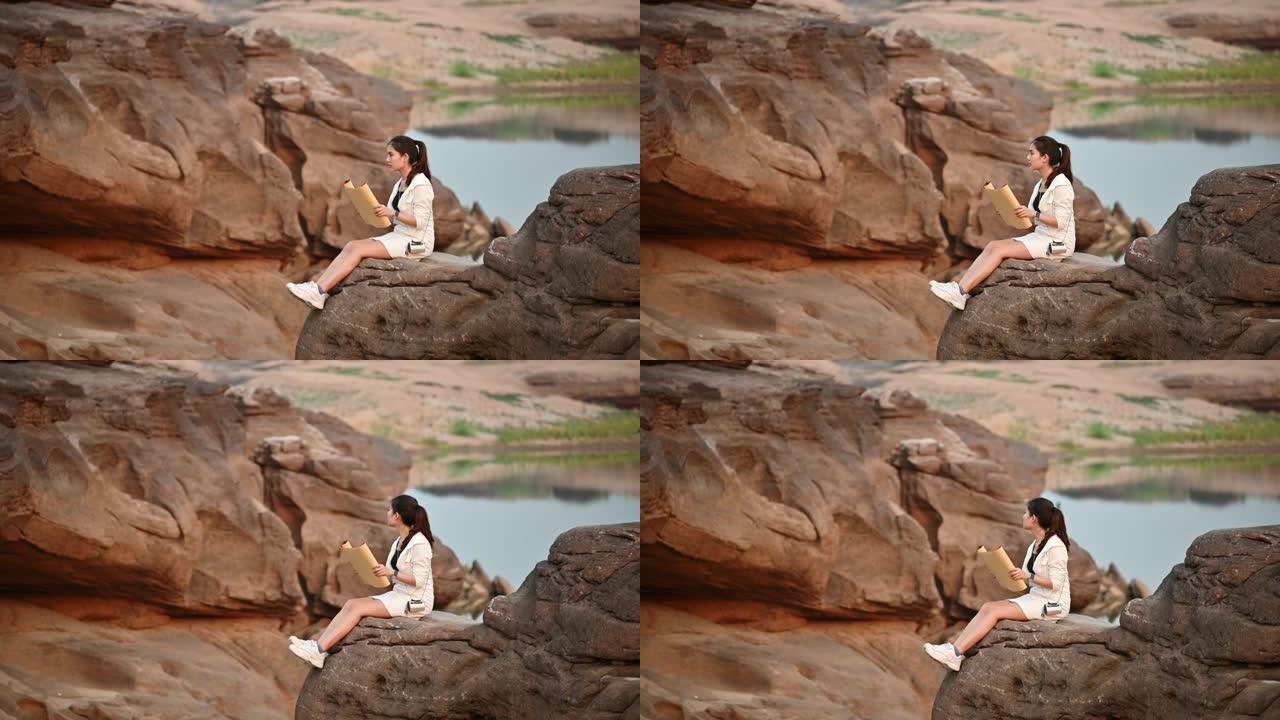 年轻的亚洲女性旅行者坐在泰国大峡谷岩石悬崖上看着纸质地图