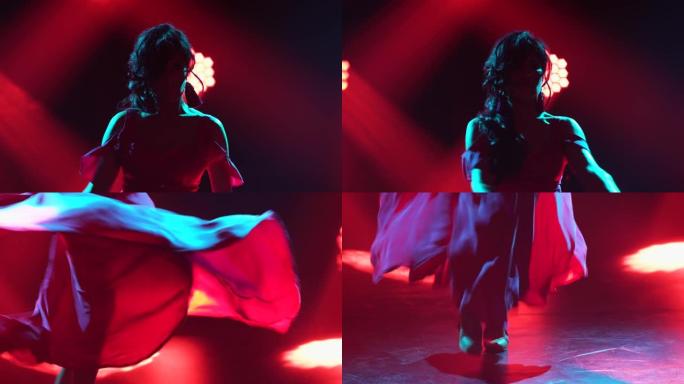 穿着红色长裙的热情黑发女人在黑暗的烟熏工作室里，在霓虹灯的背景下跳着火热的弗拉门戈舞。特写西班牙女舞