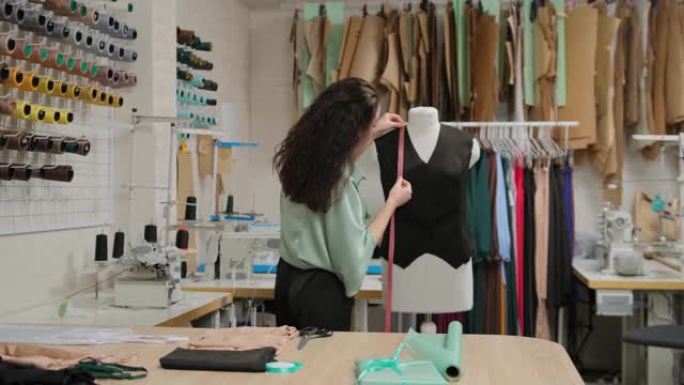 女裁缝正在用卷尺测量裁缝假人的衣服。女人专注而体贴。工作室轻巧，现代，有许多缝纫工具和物品。