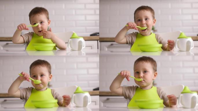 可爱的男婴坐在桌子旁，用勺子吃燕麦片的变焦镜头。宝宝在家心甘情愿地吃东西。概念快乐童年