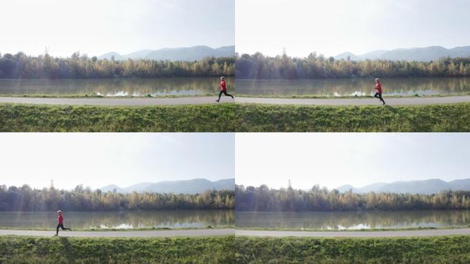 4k实时无人机镜头运动员在晴天沿河奔跑