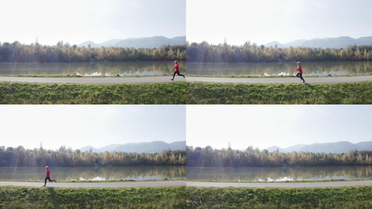 4k实时无人机镜头运动员在晴天沿河奔跑